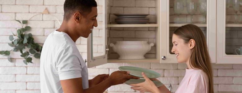 Casal guardando pratos limpos após usar sabão para lava louça na cozinha.