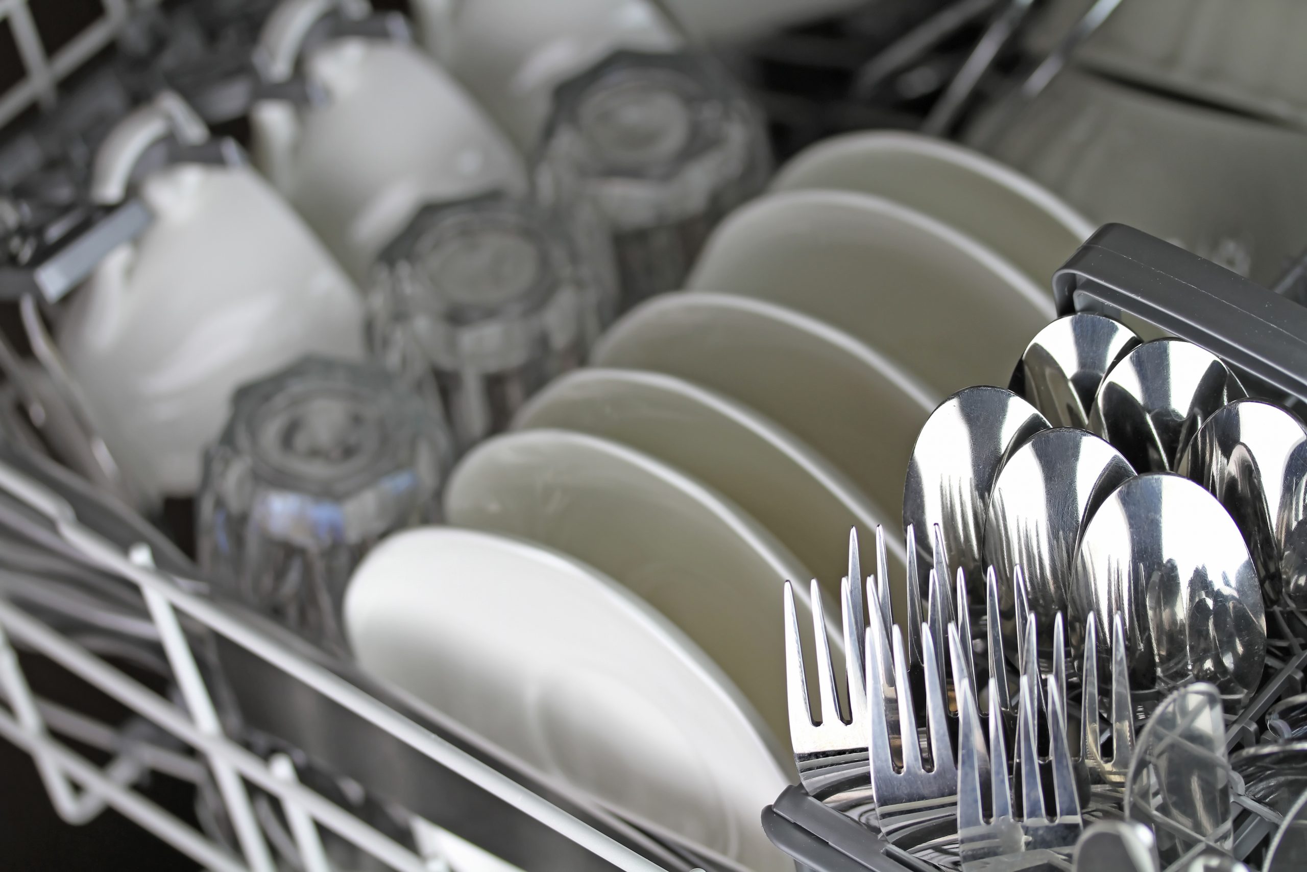 Na imagem, aparece uma máquina de lavar louça, com pratos,garfos, copo, xícara